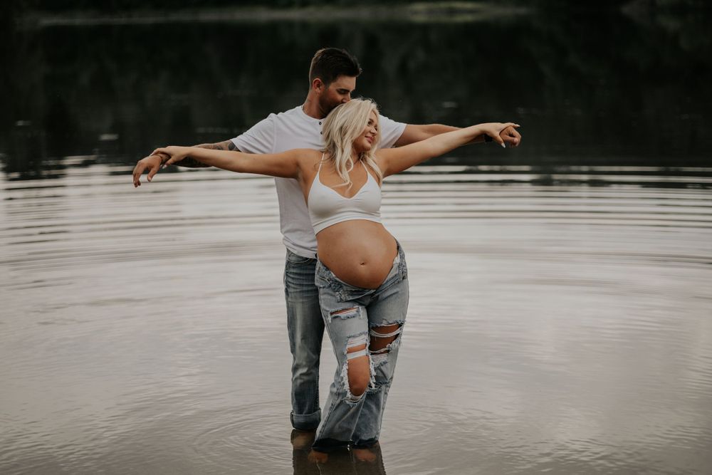 Couple standing in water during maternity photoshoot with artistic pose.