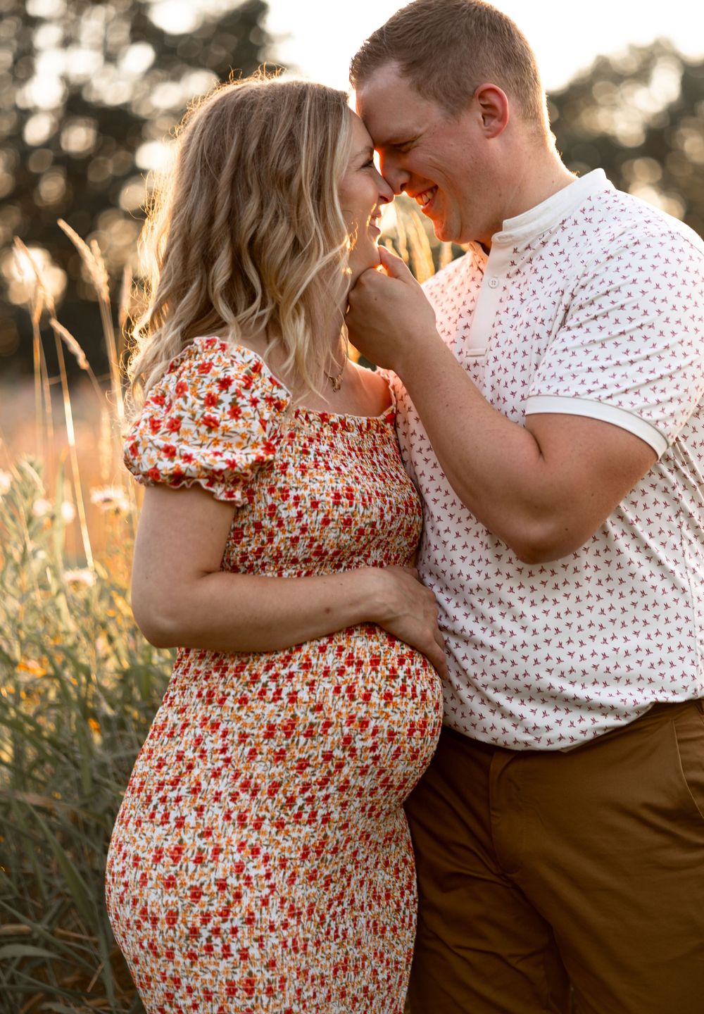 Couple in floral dress and white shirt share an intimate moment at sunset in tall grass.