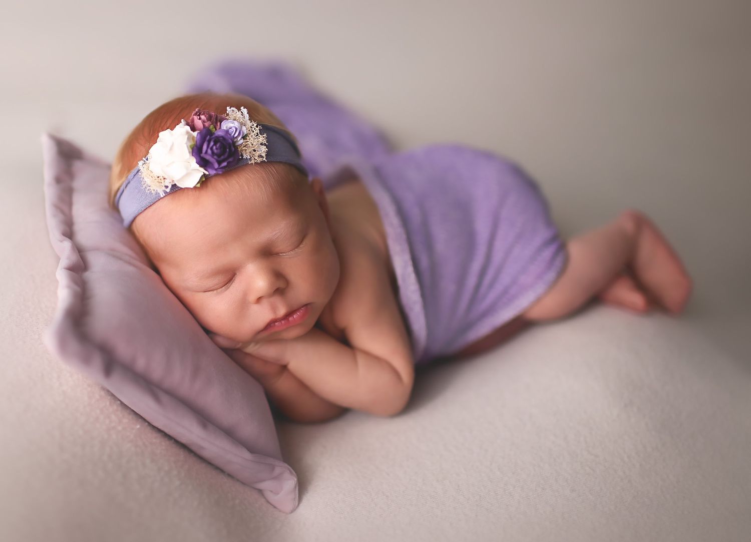 Newborn baby girl in purple sleeping in studio