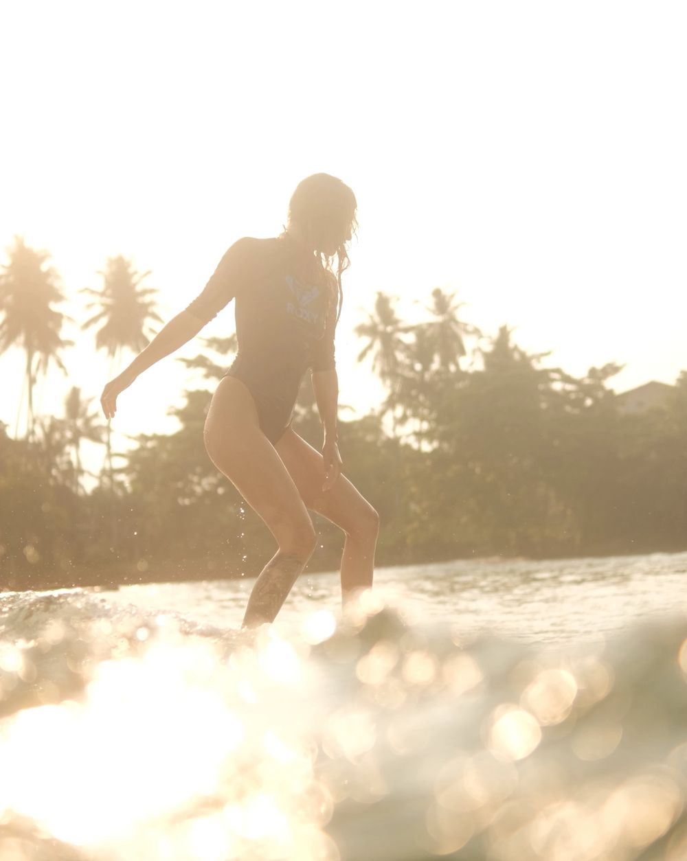 girl surfing a soft top sunset palm trees and water reflection