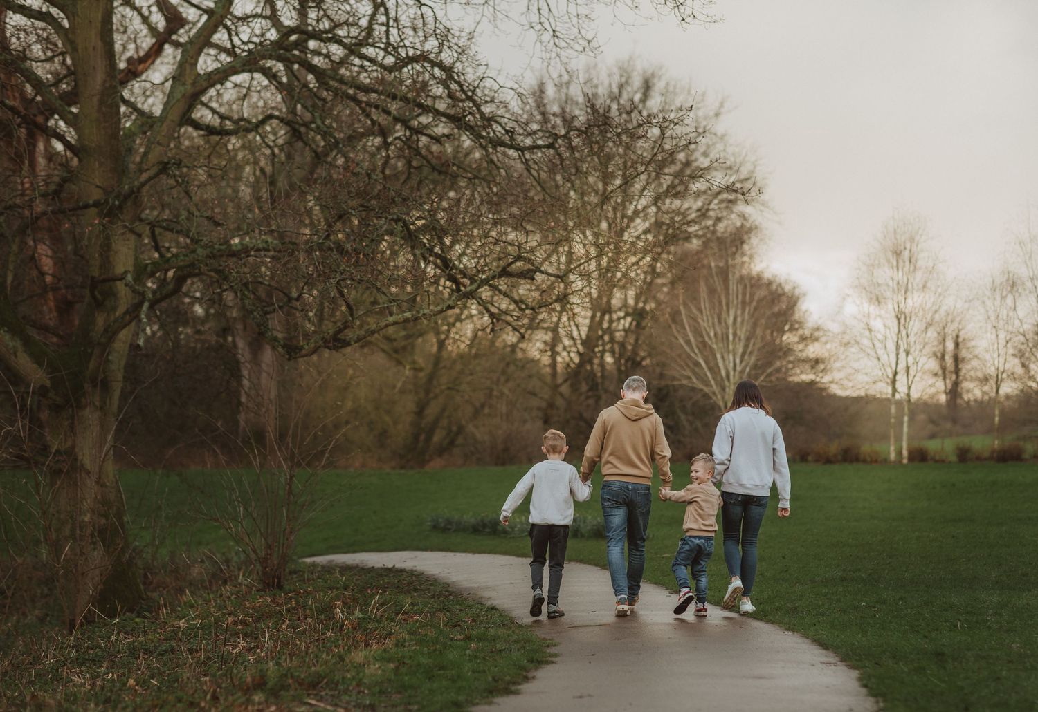 Family walking together hand in hand on paved path through park.