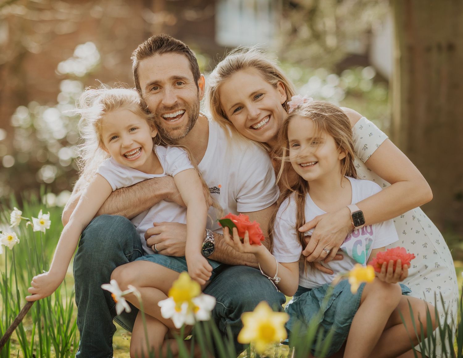 Family sitting together among spring daffodils in garden setting during golden hour.