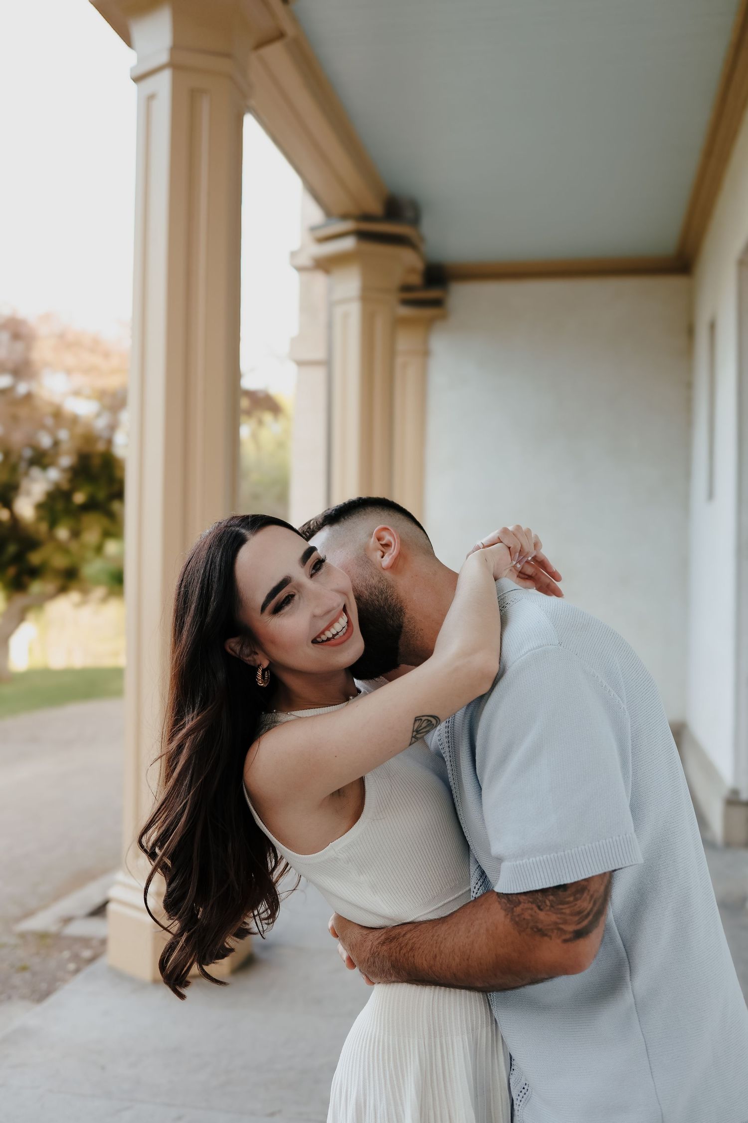 Romantic embrace captured in soft afternoon light with rustic field backdrop.