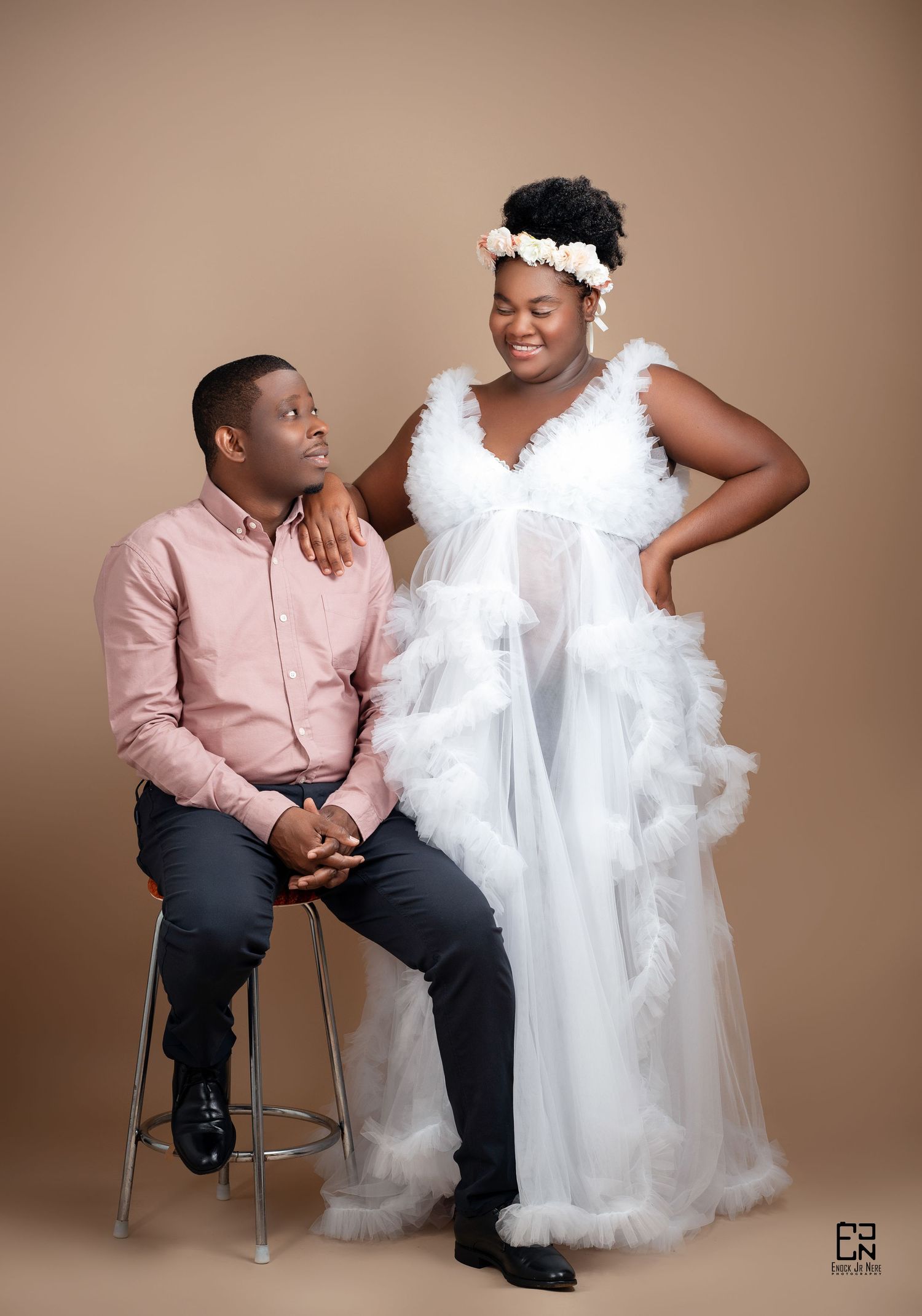 Romantic studio portrait of a couple in formal attire against a beige backdrop with person in white dress standing.