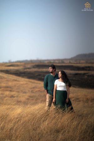 Couple standing together in golden grassland with mountains in background.