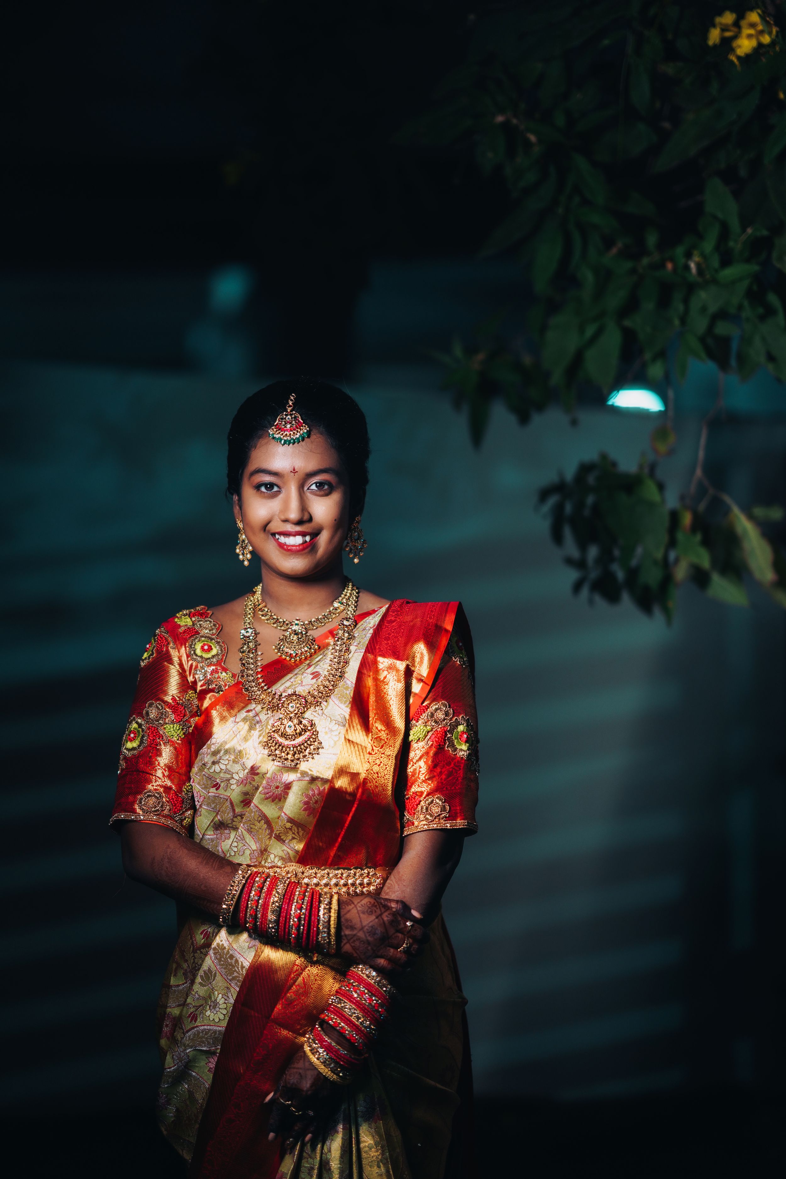 Traditional South Indian bride in red and gold silk saree with jewelry in evening light.
