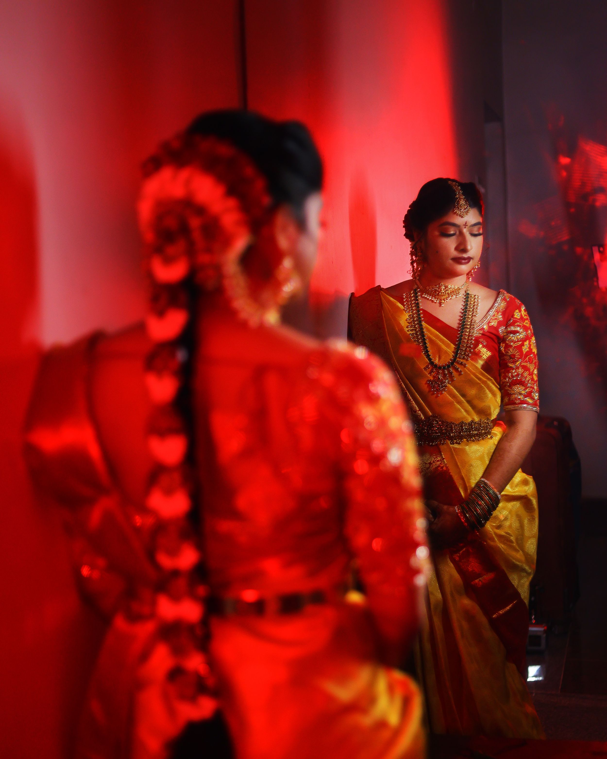 Dramatic red-lit portrait with mirror reflection in traditional South Asian attire.