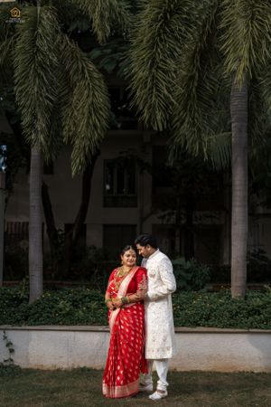 Couple in traditional Indian wedding attire posing under palm trees.