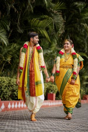 Traditional attire with yellow dhoti and floral garland shown from different walking angles against greenery background.
