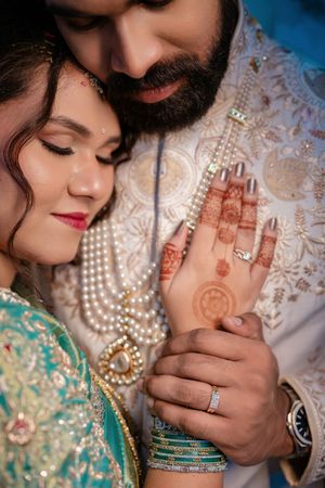 Indian bride and groom in traditional attire, showcasing intricate mehndi and pearl jewelry during wedding ceremony.