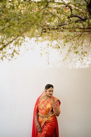 A traditional Indian outfit in bright orange and red silk with gold details stands beneath blossoming spring branches.