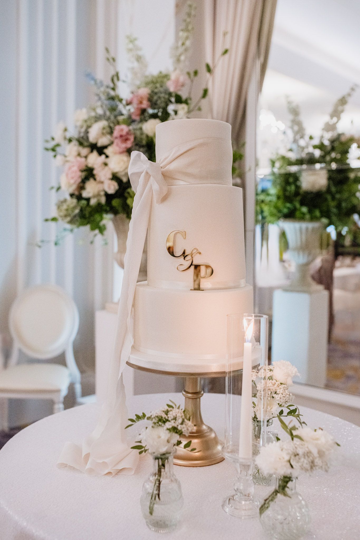Elegant white wedding cake with flowing ribbon and floral decorations on a golden cake stand.