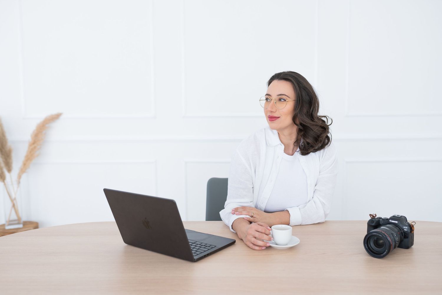 Person in white working on laptop with camera nearby in bright setting.