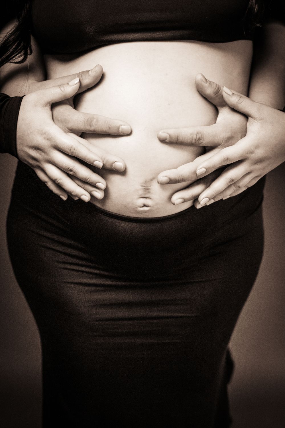 Black and white maternity photo showing hands cradling pregnant belly.