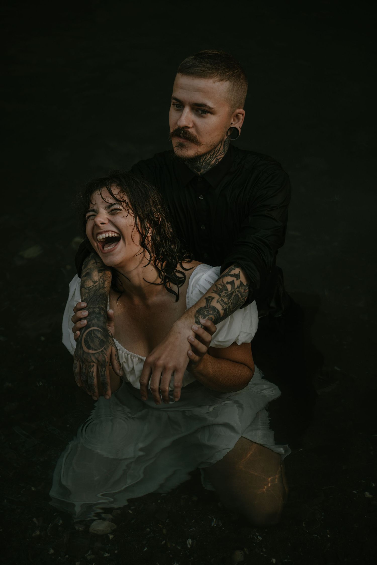 Moody artistic portrait of tattooed couple in dramatic dark setting.