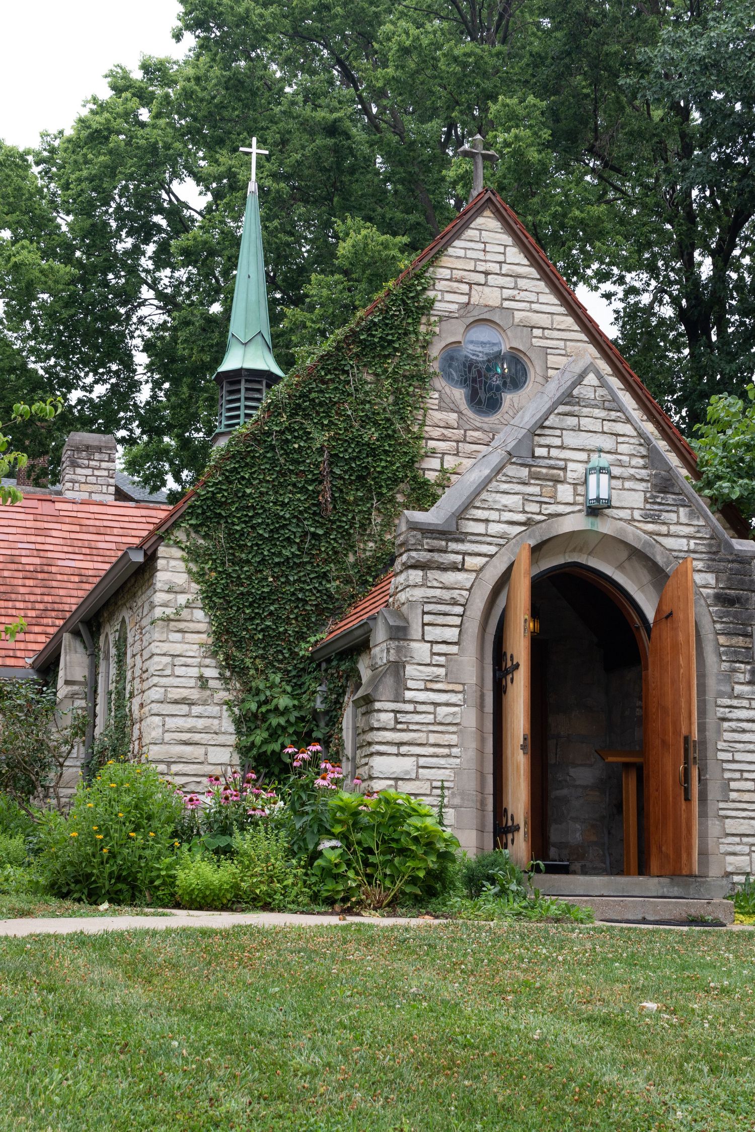 Row of small stone chapel buildings with wooden doors and red roofs on grassy hillside.