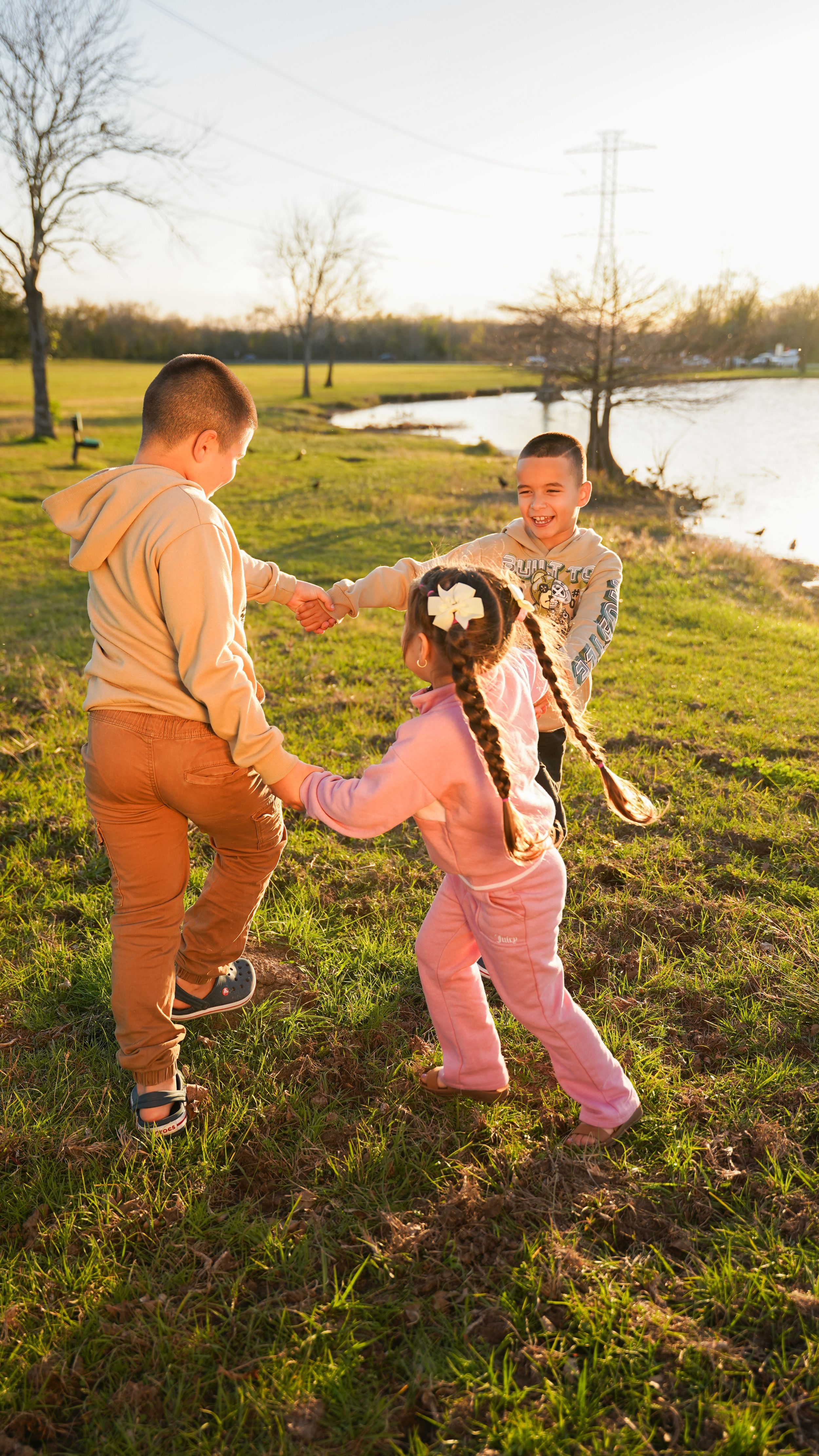 Children playing together in a park at sunset near a lake on a grassy hill in warm golden light.