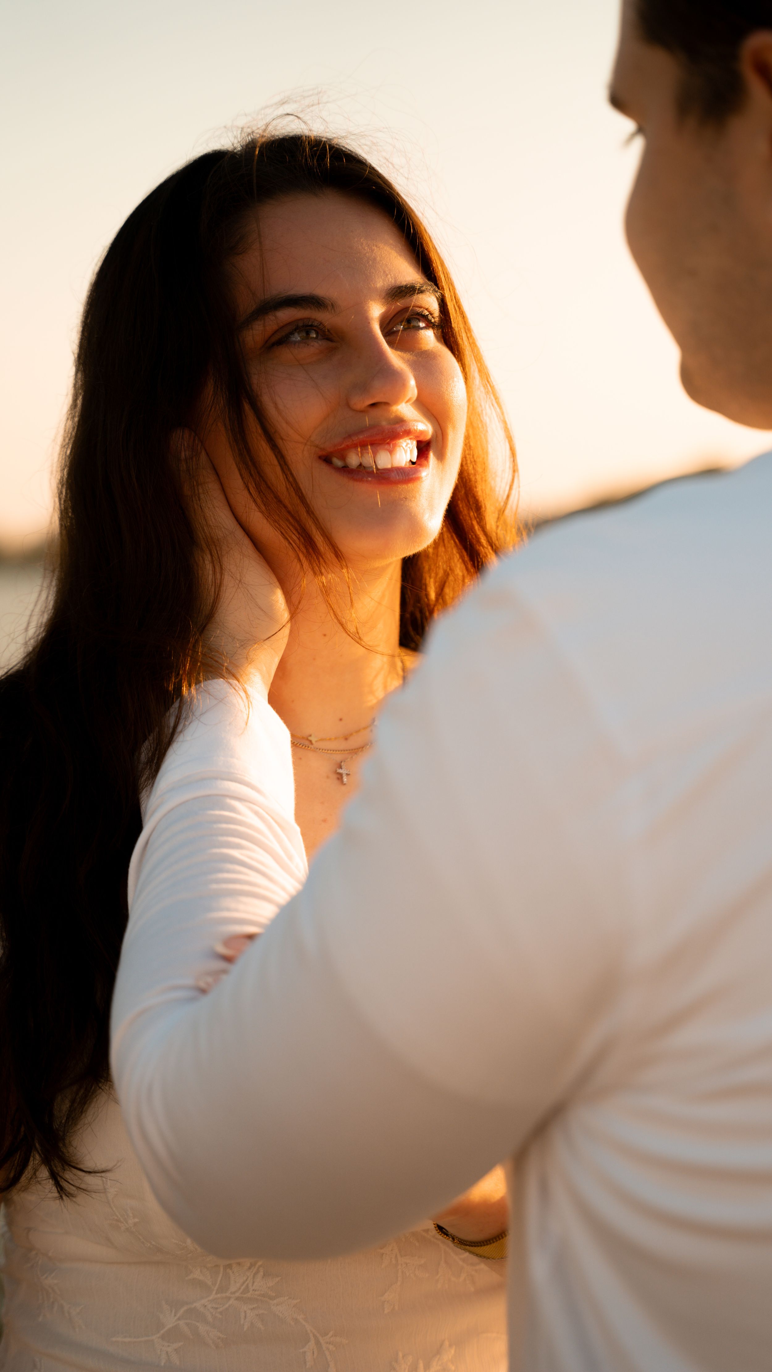 A couple in white clothing share an intimate moment in warm sunset lighting with soft focus and natural glow.