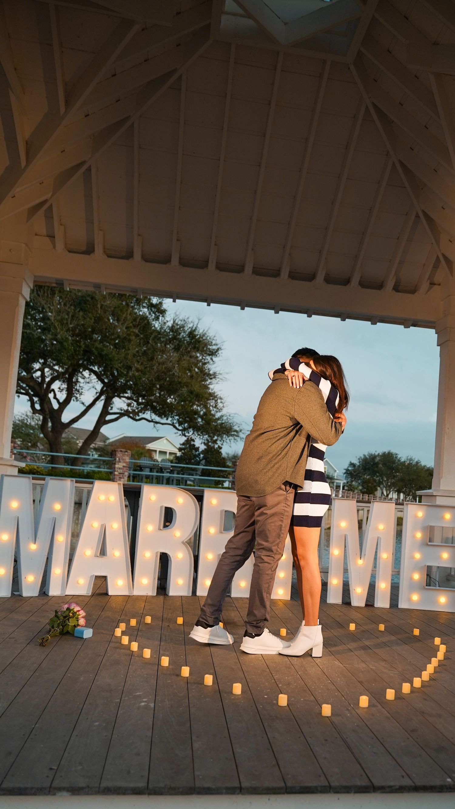 An intimate proposal scene on a deck with twinkling lights in the evening.