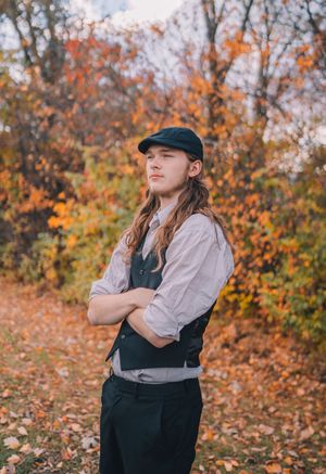 A person in vintage-inspired clothing poses playfully against a backdrop of vibrant autumn foliage.