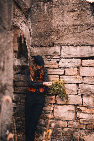 Stone wall texture with rustic layered rocks and small green plant growing between the cracks in moody lighting.