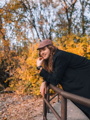 A person in a black coat performs a playful plank pose on a wooden railing during autumn with golden foliage in background.