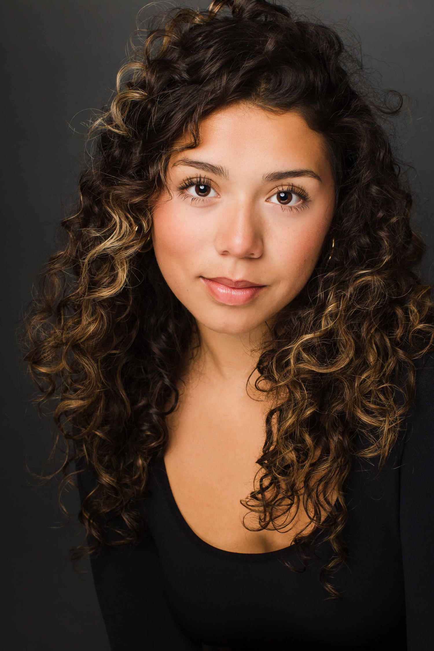 Studio portrait of a woman with natural curly hair highlighted with caramel tones.