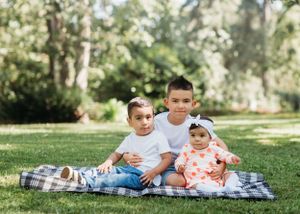 Three siblings sitting together on plaid blanket for outdoor portrait session.