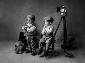 Black and white portrait of two children in vintage attire posed with an old-fashioned camera setup.