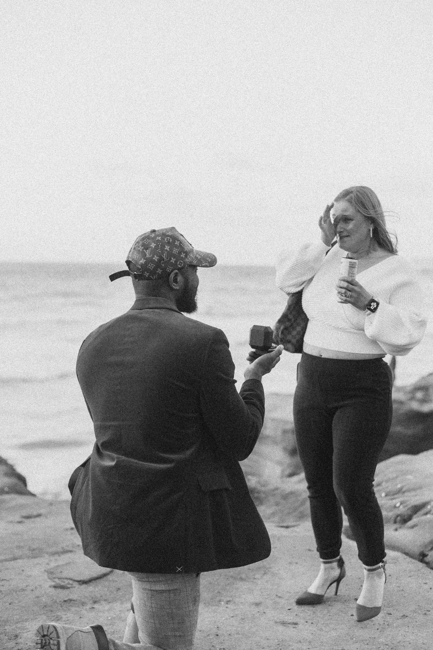 Black and white photo of a surprise proposal moment on coastal rocks.