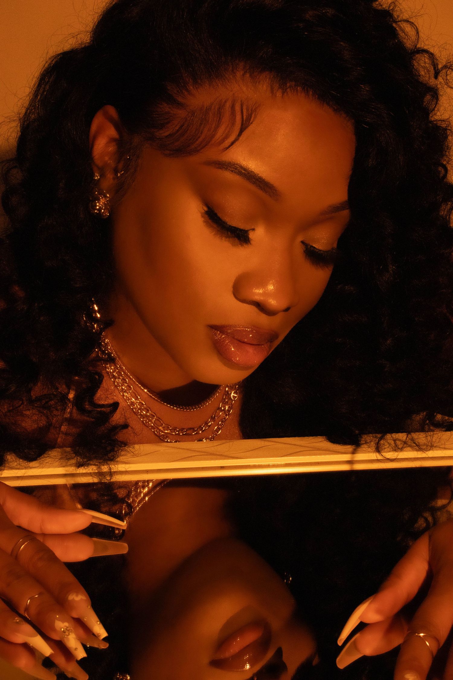 Beautiful portrait in warm amber lighting with curly hair, glam makeup, choker necklace and reflective surface below.