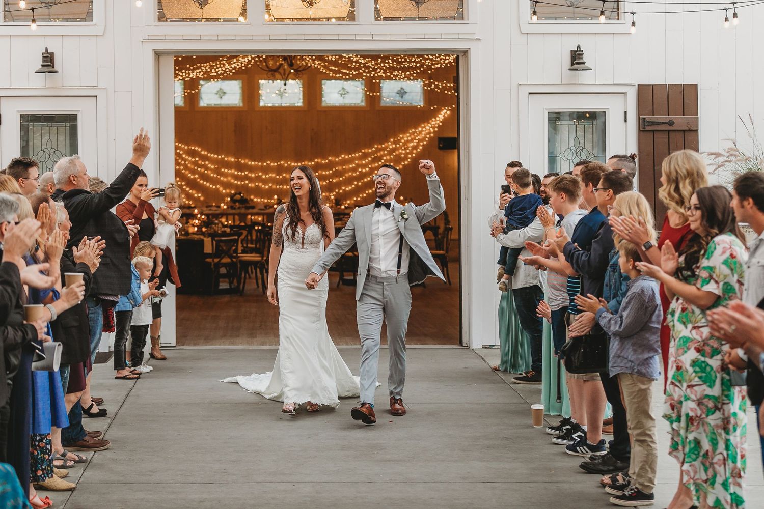 Newlyweds celebrate with a joyful exit while guests cheer in an indoor venue with string lights and rustic decor.