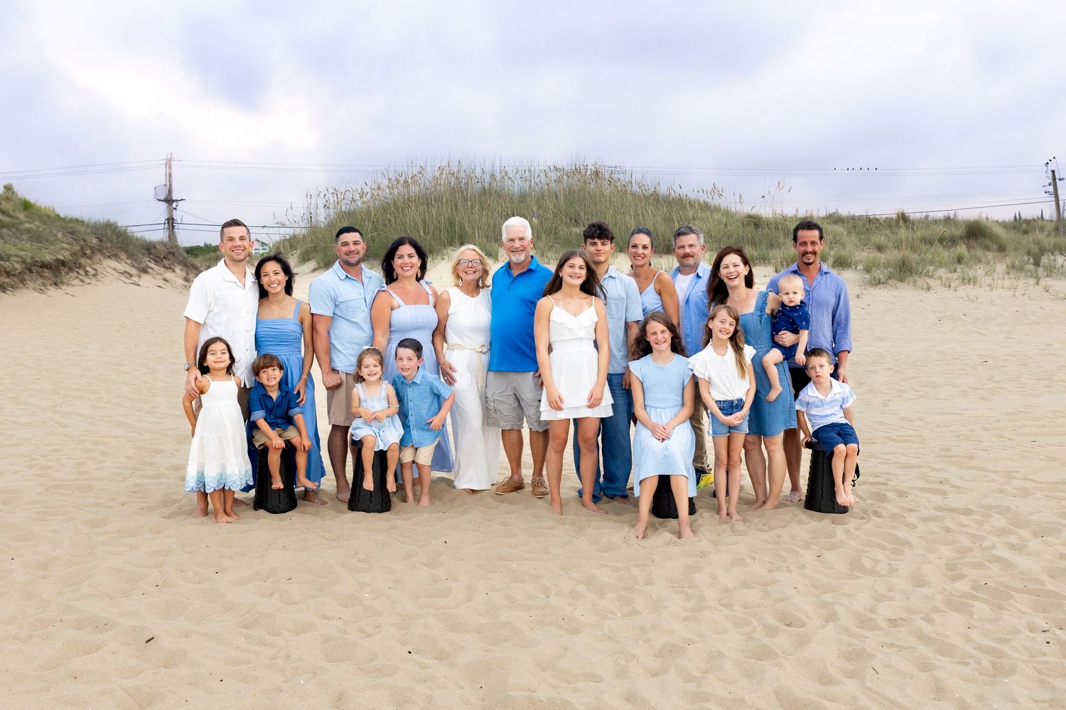 Large group of people wearing coordinated blue and white outfits posing together on a sandy beach during a photo shoot.