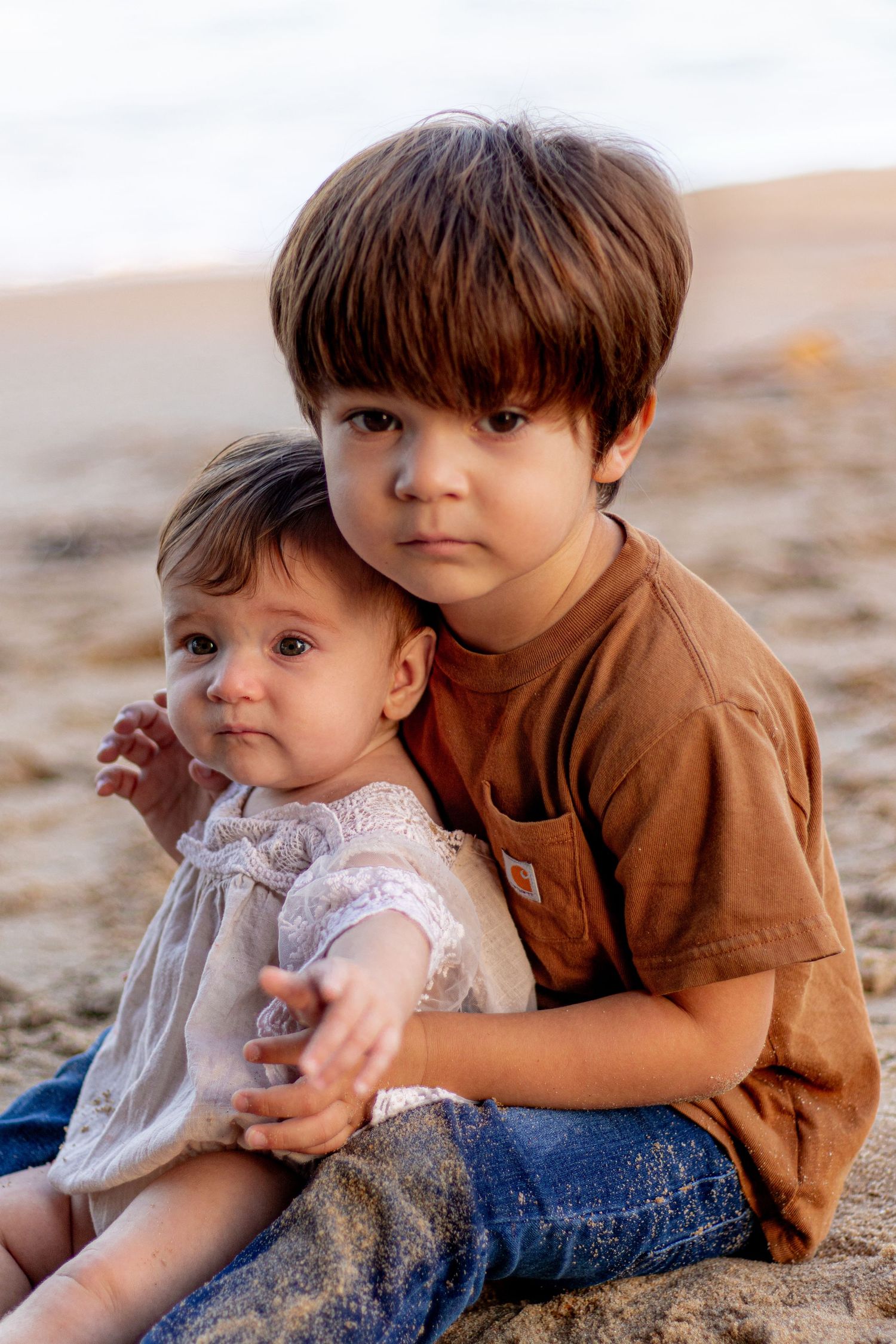 Two siblings sharing a sweet moment together on the beach at sunset.