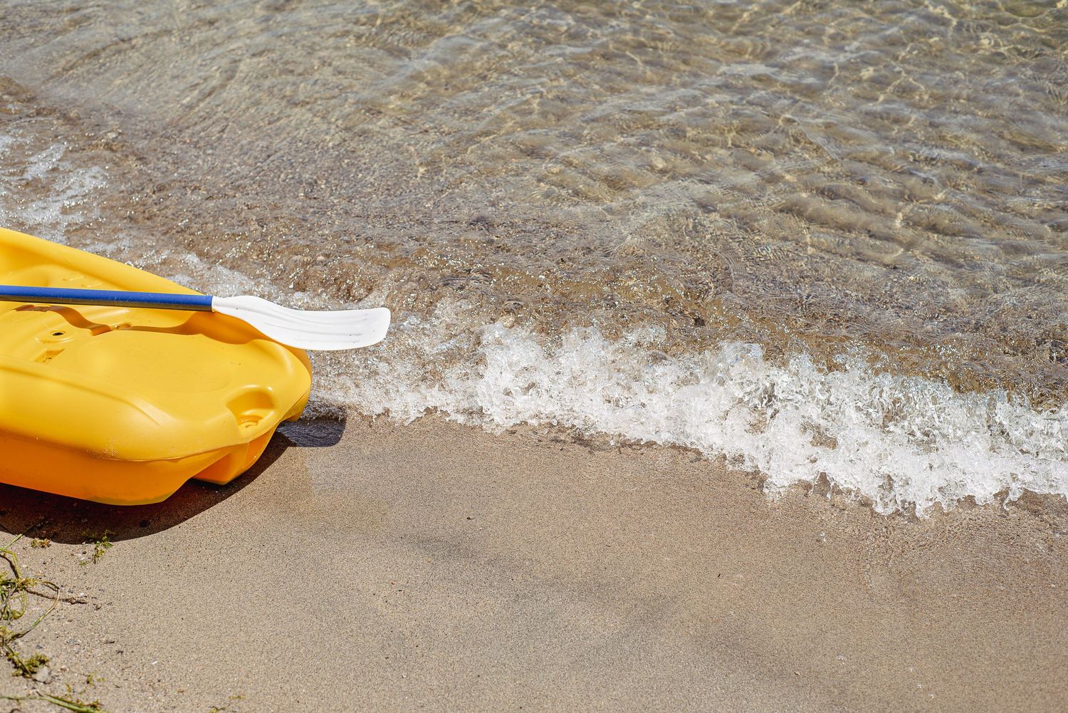 Yellow kayak paddle lying on sandy beach with gentle wave approaching.