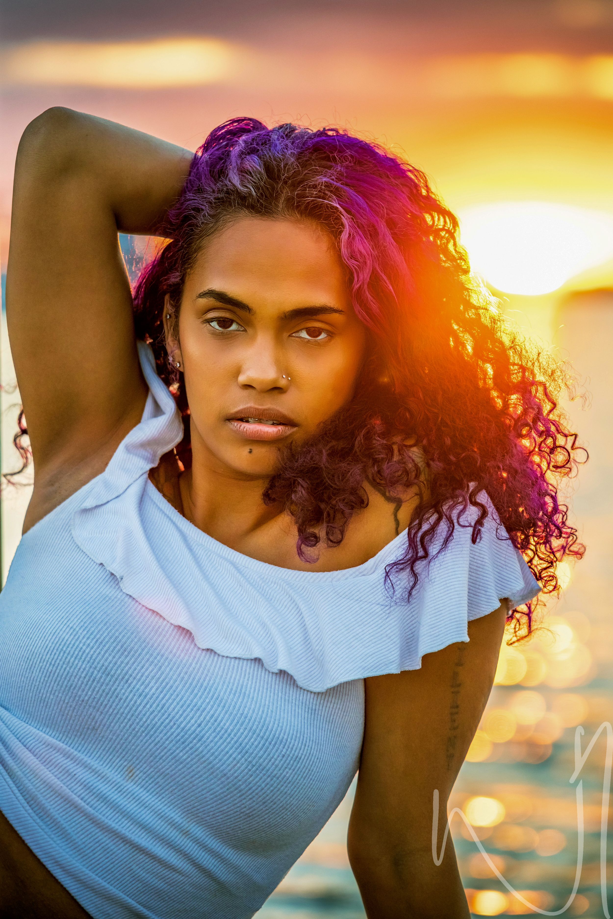 Beach portrait with purple curls and light blue top during golden hour sunset.
