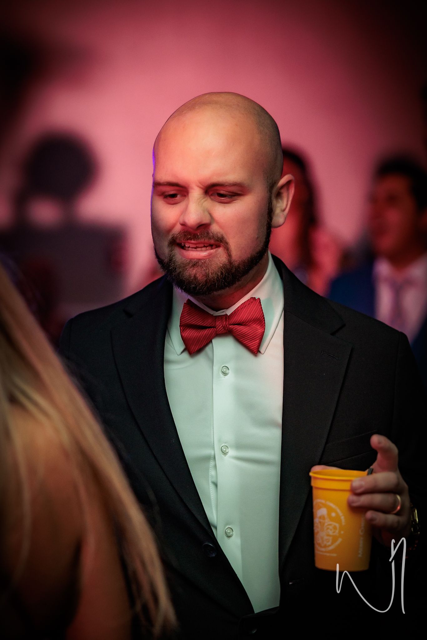 A sequence showing someone in formal attire with a red bow tie holding a yellow drink cup in dim lighting.