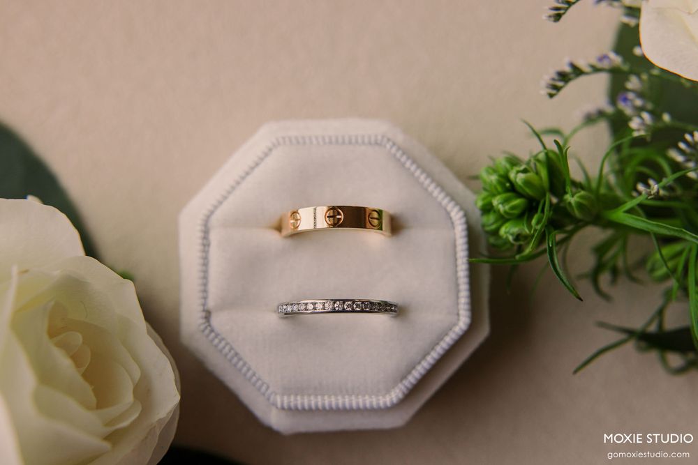 Wedding rings displayed on white cushions with elegant floral decor and greenery in a romantic setting.
