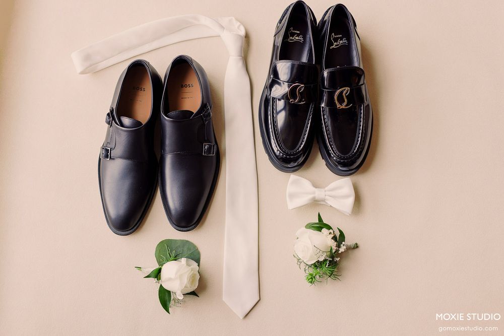 A collection of black leather formal dress shoes arranged in a row with white floral decorations between them.