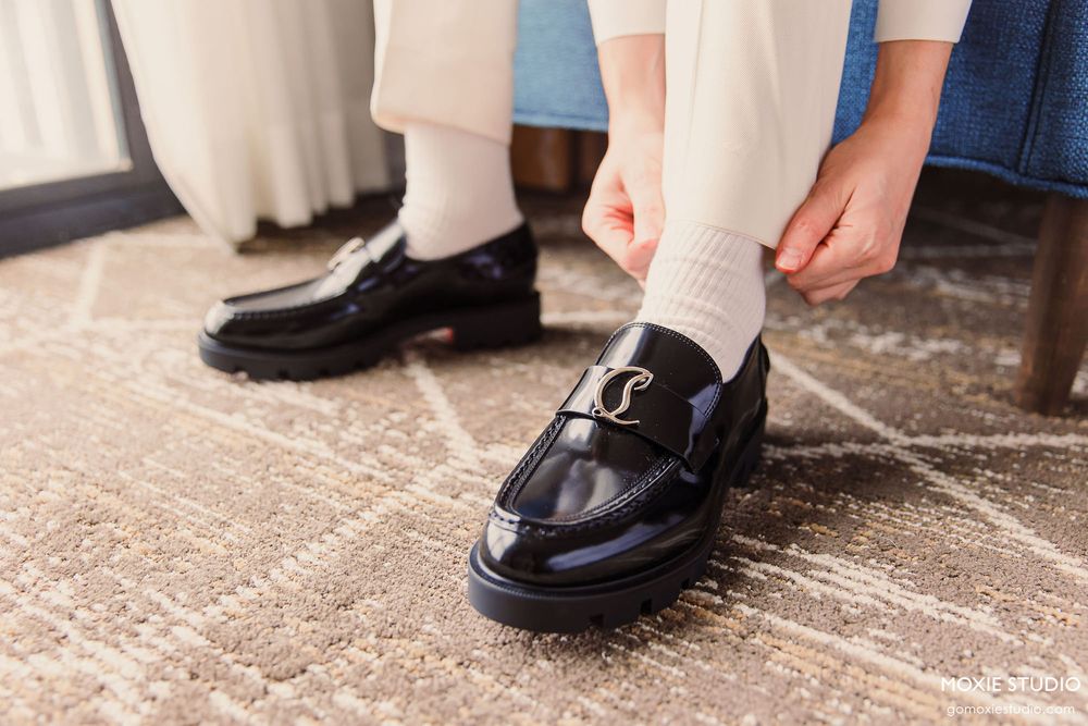 Close-up view of black leather loafers with white socks on a textured stone surface.
