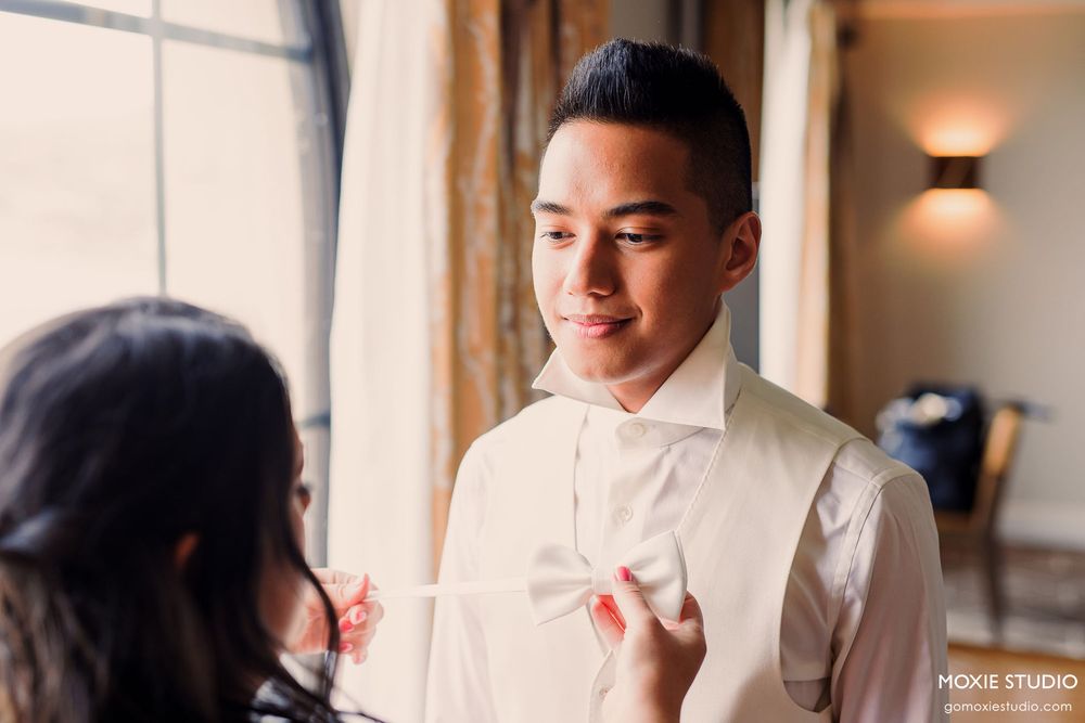 A couple in formal wedding attire share an intimate moment by a sunlit window.