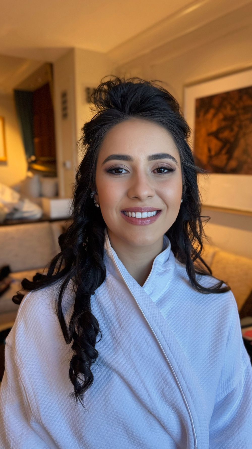 A woman in a white robe with wavy dark hair smiles warmly at the camera.