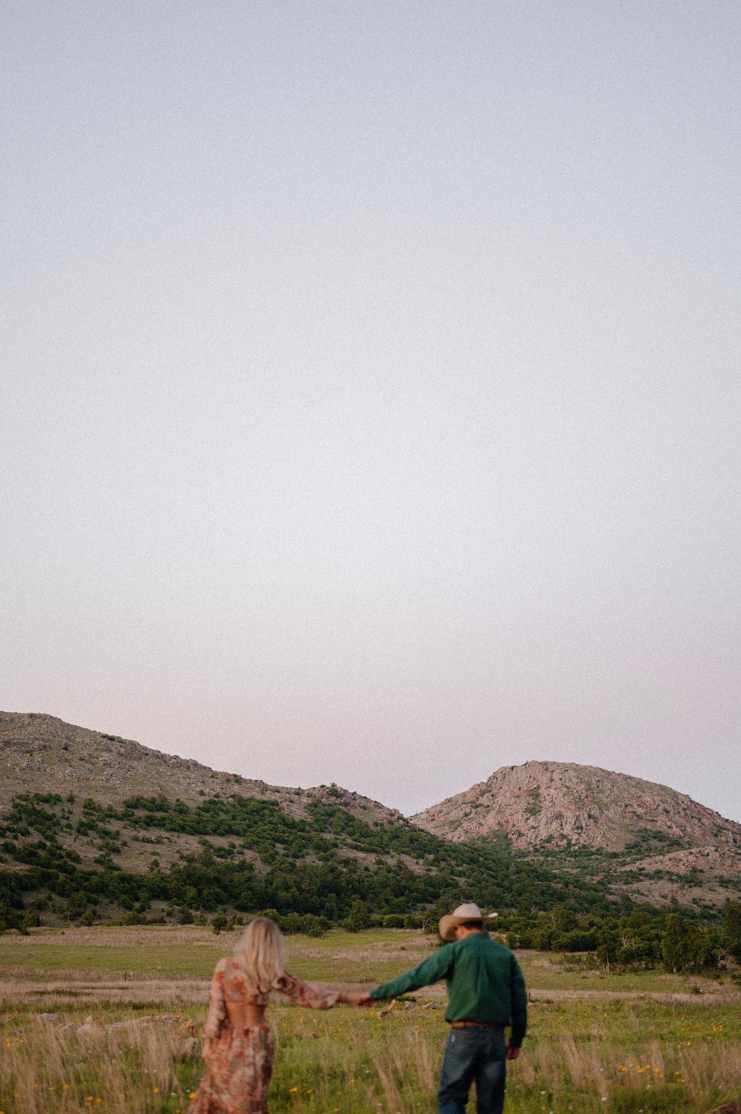 Couple walking hand in hand through scenic mountain landscape at dusk. Oklahoma Wedding Photographer