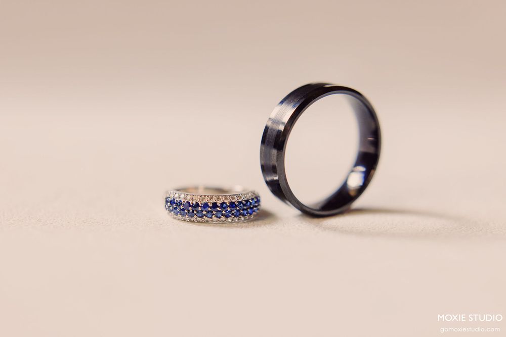 Two elegant wedding rings, one with sapphire stones and one plain band, displayed on a light neutral background.