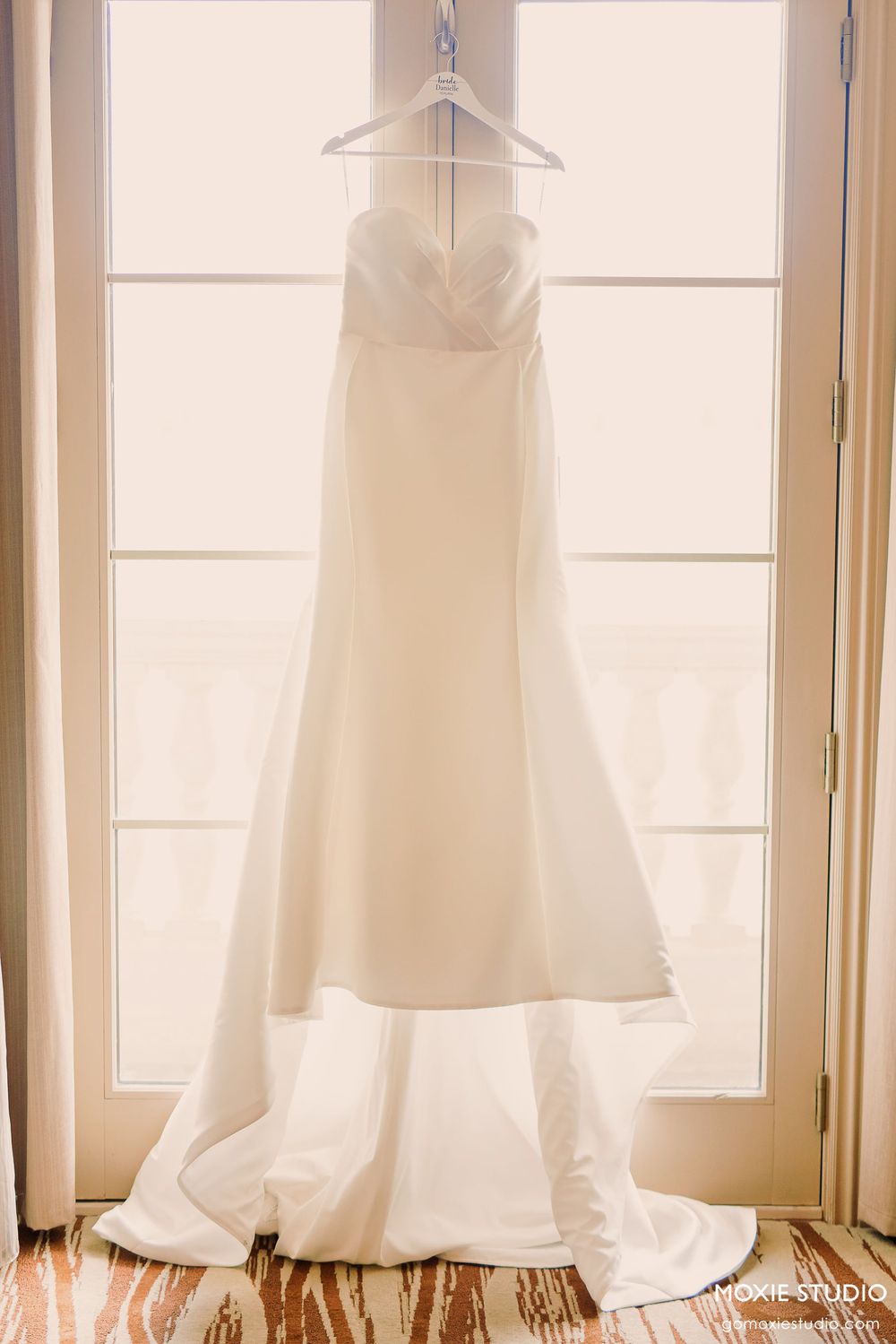 Multiple white wedding dresses hanging on display in a sunlit room with large windows.