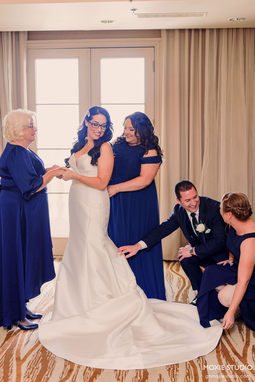 Wedding party gathered in an elegant room with white and navy blue attire during a special moment.