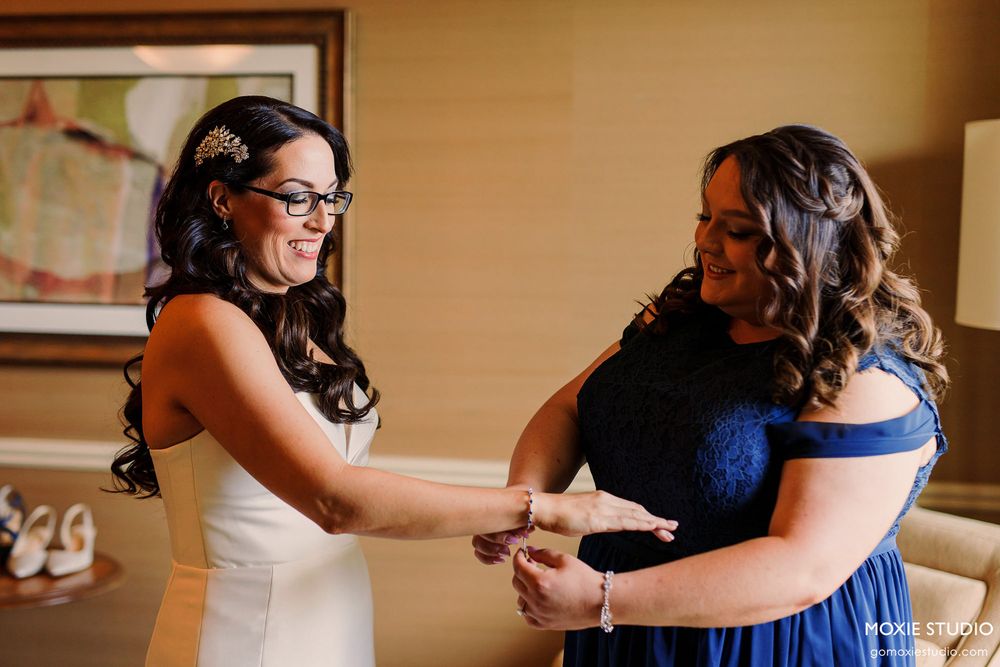 Two women in formal attire share a joyful moment while getting ready for a special occasion.