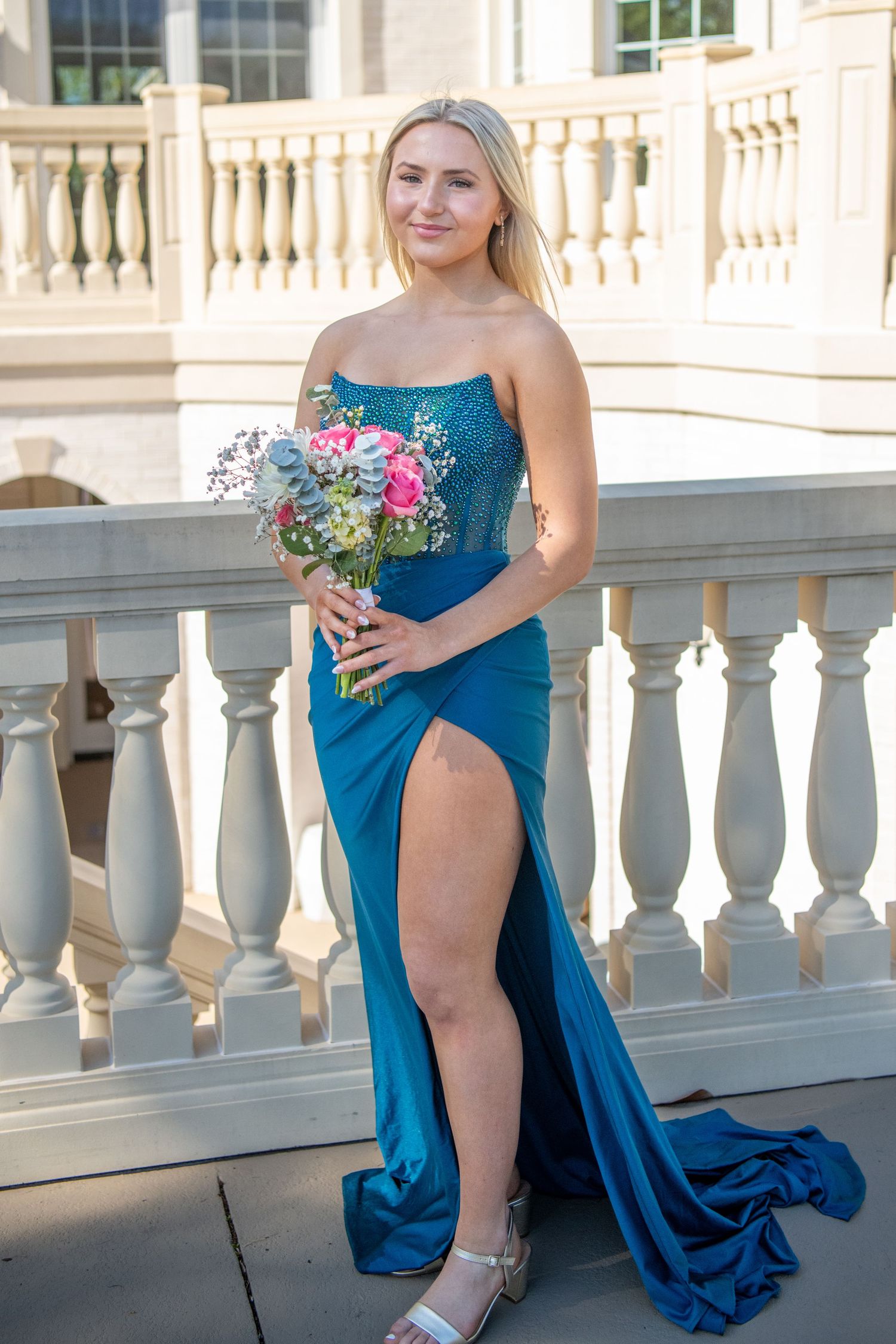 Wedding party member in a blue gown poses dramatically on an elegant white balcony.