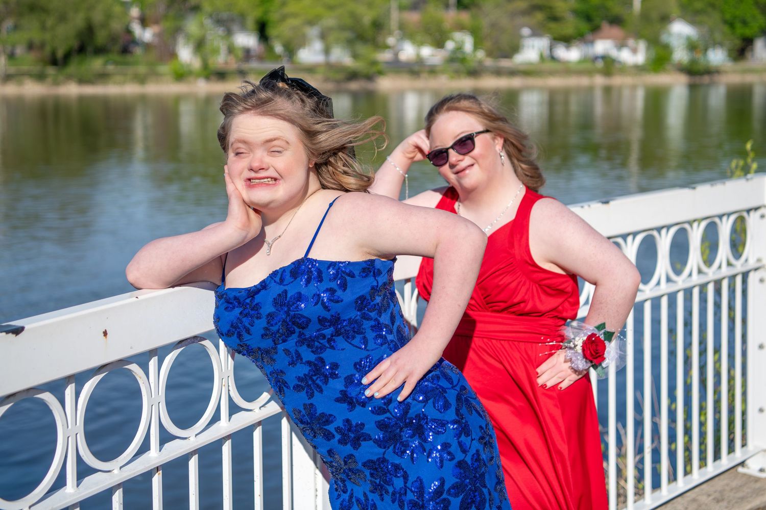 Friends enjoying a PROM photoshoot by the water with decorative white railings and trees in the background.