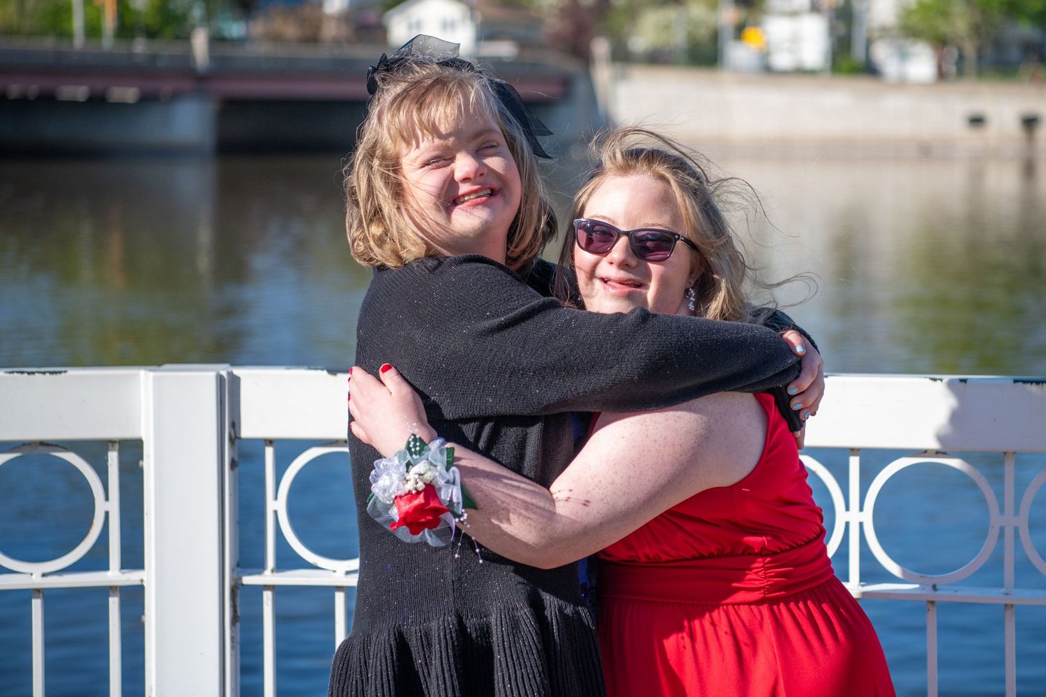 Two friends sharing a joyful embrace by waterfront railing.